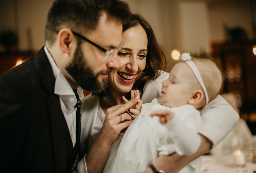 Sesja chrztu Rawicz - uśmiechnięci rodzice trzymają niemowlę na rękach w kościele