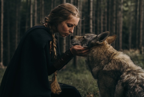 Sesja artystyczna - portret kobiety w stroju fantasy całującej wilka na tle lasu