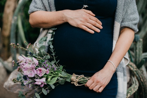 Sesja ciążowa - kobieta z ręką położoną na brzuszku i bukietem kwiatów