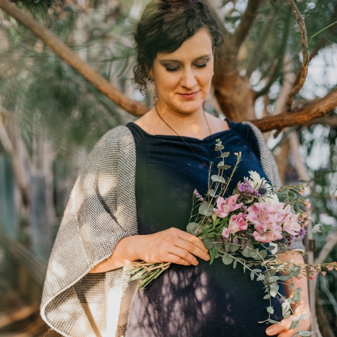 Sesja ciążowa - kobieta w granatowej sukni z bukietem kwiatów na tle egzotycznej roślinności