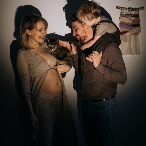 Sesja ciążowa - mąż trzymający na ramionach synka dotyka brzuszka kobiety