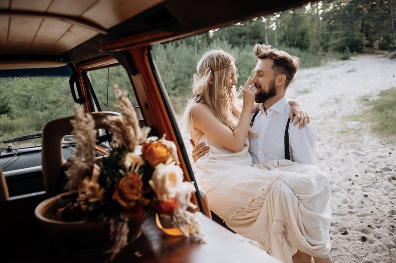 Zdjęcia ślubne nad morzem - Pan Młody trzyma Pannę młodą na rękach i niesie do kampera