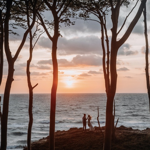 Zdjęcie ślubne pary młodej w oddali na tle morza i zachodzącego słońca