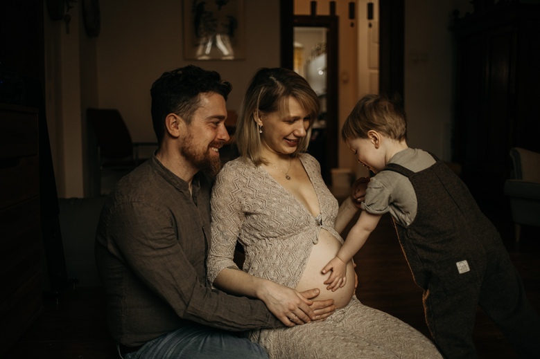 Sesja ciążowa w Poznaniu - dziecko dotyka brzucha mamy, którą obejmuje jej mąż