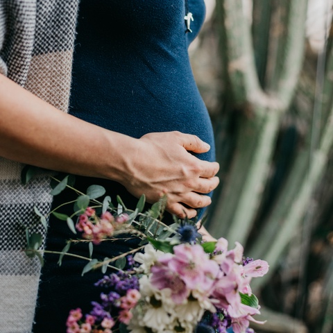 Sesja ciążowa - kobieta stojąca profilem z bukietem kwiatów