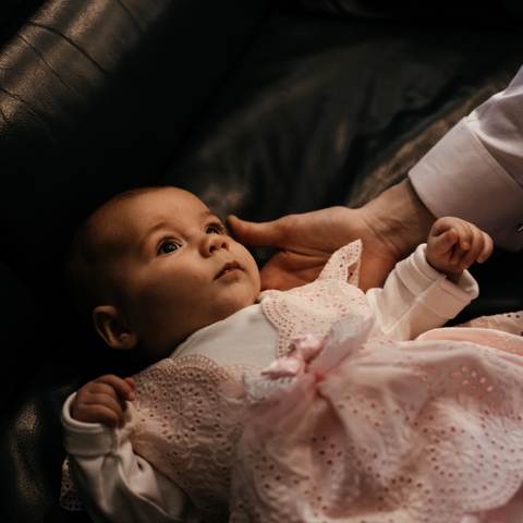 Sesja chrztu - rodzic wyciąga rękę po niemowlę leżęce na kanapie