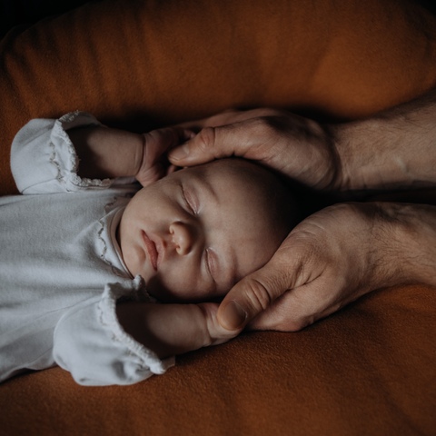 Sesja noworodkowa - portret z główką leżącego dziecka w rękach ojca